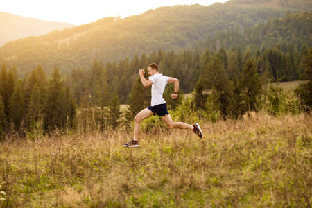 Running fitness man sprinting outdoors with beautiful mountains landscape on background. Caucasian sport male runner training for marathon.の写真素材