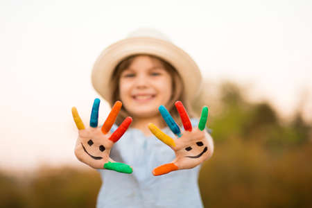 Happy smiling little girl with hands in paint play outdoor in summer park. Focus on handsの写真素材