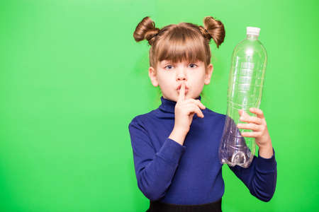 Funny little girl with shocked face and hand near head holding plastic bottles and looking confused at camera isolated over green backgroundの写真素材