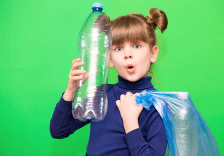 Girl hold trash bag and plastic bottle and shows interest in environmental issues isolated on green background. Child accustomed to bear responsibility for garbage since childhood. Plastic trash sorting conceptの写真素材