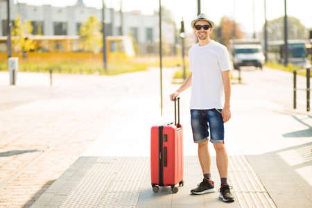 Traveling guy with suitcase wearing smart style clothes waiting for transport. Copy spaceの写真素材