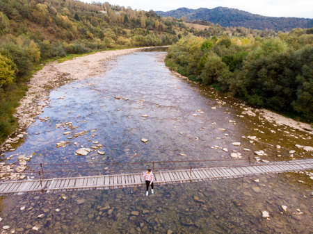 Aerial top drone view of woman traveler on wooden bridge over mountains river, autumn travel concept.の写真素材