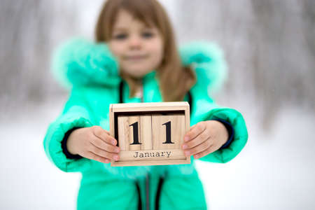Little girl hold wood cube with date month outdoor in winter. January 11th. Day 11 of monthの写真素材