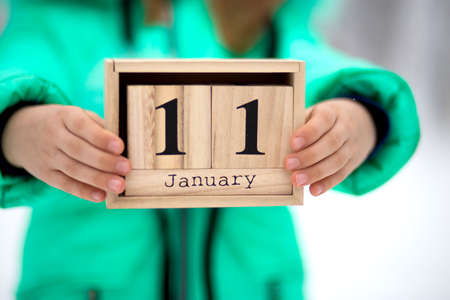 Little girl hold wood cube with date month outdoor in winter. January 11th. Day 11 of monthの写真素材