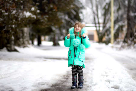 Funny little girl having fun in beautiful winter park during snowfallの写真素材