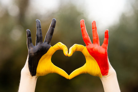 Kid hands painted in Belgium flag color show symbol of heart and love gesture on nature backgroundの写真素材