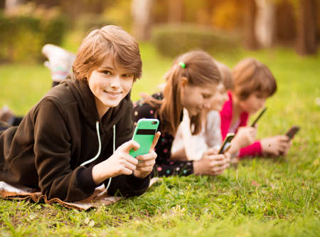 Portrait of cute smile child girl use mobile phone and laying with friends on grass at spring park. Selective focusの写真素材