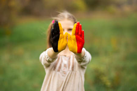 Child girl show hands painted in Belgium flag colors walking outdoor, focus on handsの写真素材