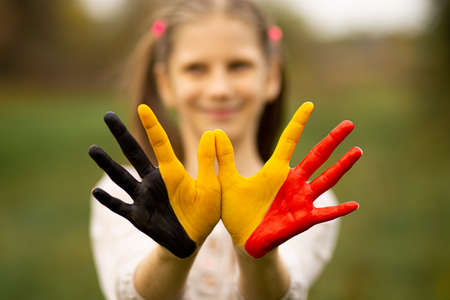 Child girl show hands painted in Belgium flag colors walking outdoor, focus on handsの写真素材