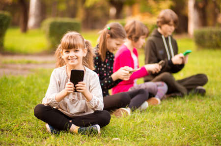 Outdoor portrait of little girls and boys playing with phones . High quality photoの写真素材