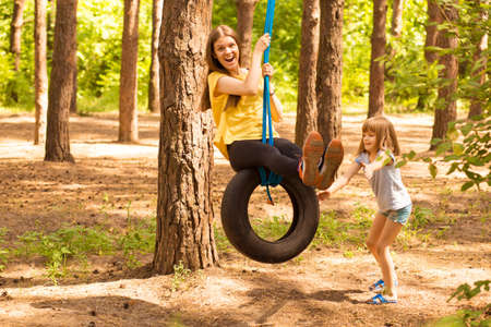 Happy child daughter pushing mother on tire swing in autumn garden.の写真素材