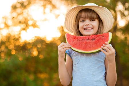 Adorable little preschool kid boy with blond hairs eating watermelon in summer holidays outdoor. Funny happy child smiling and tasting healthy fruit snack on sunny day.の写真素材