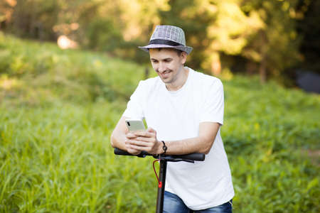 Young man in hat use mobile phone, book online rental electric scooter in city. Innovative transportの写真素材