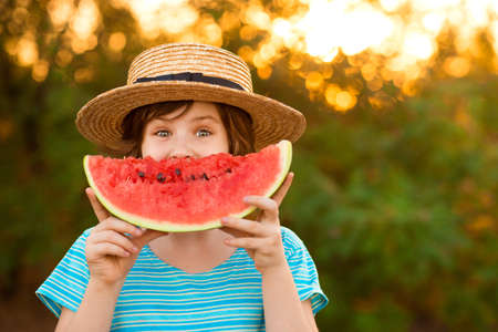 Adorable little preschool kid boy with blond hairs eating watermelon in summer holidays outdoor. Funny happy child smiling and tasting healthy fruit snack on sunny day.の写真素材