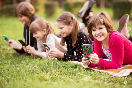 Outdoor portrait of little girls and boys playing with phones . High quality photoの写真素材