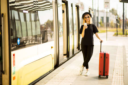 Young tourist woman use smart phone with suitcase and wear total black. Traveller girl call taxi on train stationの写真素材