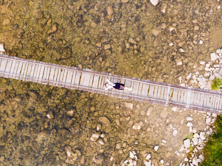 Top drone view of woman with hands up in dress laying down on wooden bridge over river. High quality photoの写真素材