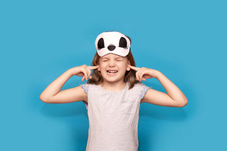 Portrait of stressed child with sleeping mask isolated on blue background. Little girl cover her...