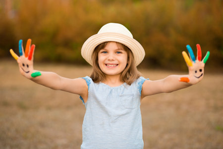 Happy smiling little girl with hands in painted in funny face play outdoor in summer park.の写真素材