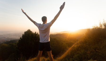Silhouette of young man raises his hands up to sunset or sunrise on on top of hill in the summerの写真素材