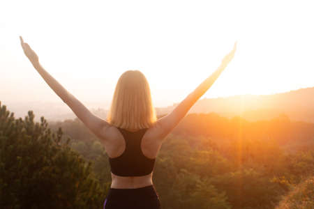 Asian woman rise hand up on top of hill with sunset sky abstract background. Girl standing and looking far away at sunrise timeの写真素材