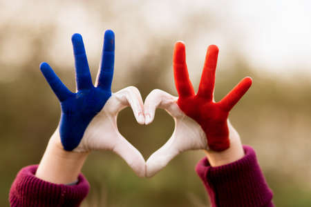Love and happiness concept. Cute child forming heart gesture with hands outdoors on nature sunset bokeh background. Heart shape of kids hand painted in france flag colors, kids body language, childrens love concept.の写真素材