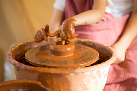 Master class for the child. Teacher hands show to kid how make ceramics dishes on potter wheel. Artist works with clay. Little girl sculpt cup clayの写真素材