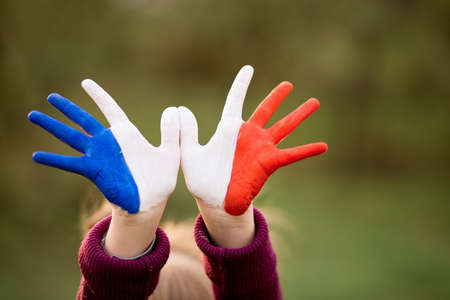 Freedom France concept. Cute child forming flying bird gesture with painted in France colors hands at bright sunset background. July 14, National Day of Franceの写真素材