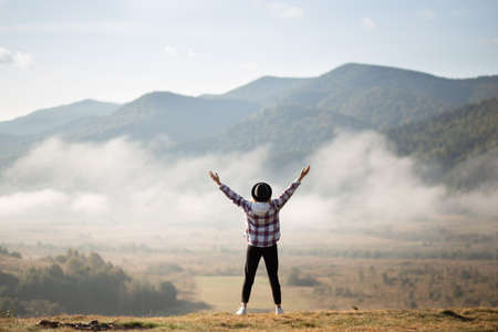 Happy girl standing on top of mountains with raised arms and enjoy amazing the view. Silhouette female hiker on top of a summer mountain covered in white clouds.の写真素材