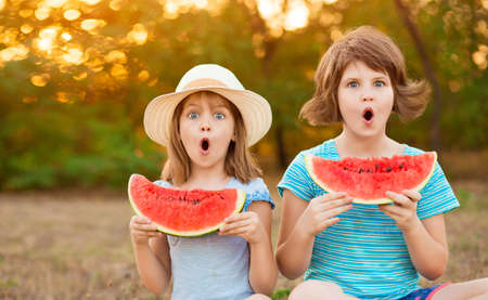 Adorable child girls with wonder face and with watermelon in hands think about question, thoughtful about confusing idea. Summer holidaysの写真素材