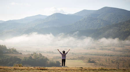 Happy girl standing on top of mountains with raised arms and enjoy amazing the view. Silhouette female hiker on top of a summer mountain covered in white clouds.の写真素材
