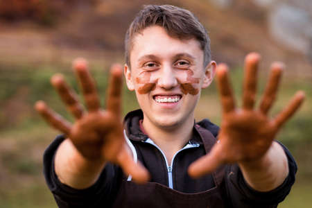 Joyful portrait of man potter with clay dirty face. Young handsome man on pottery workshop of ceramic for children. Hobby and leisure conceptの写真素材