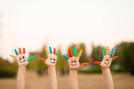 Children hands in colorful paint with funny smile face outdoor in summerの写真素材