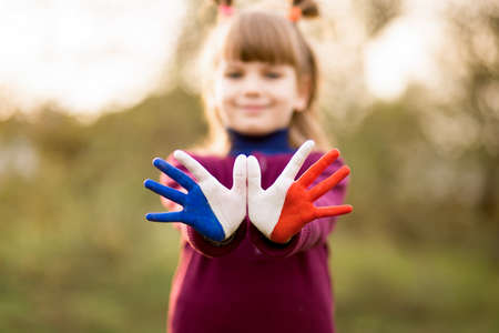 Freedom France concept. Cute child forming flying bird gesture with painted in France colors hands at bright sunset background. July 14, National Day of Franceの写真素材