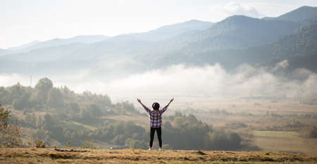 Happy girl standing on top of mountains with raised arms and enjoy amazing the view. Silhouette female hiker on top of a summer mountain covered in white clouds.の写真素材
