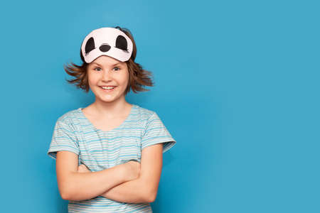 Happy portrait of cute adorable kid. Child girl in mask for sleeping. beautiful girl want to sleep, isolated on blue background. High quality photoの写真素材