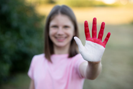 Girl with open hand raised, painted in Indonesia flag color, focus on hand. Girl show stop gesture with hand. Indonesian Independence Day, Hari Kemerdekaan, 17 August. National Day of Monaco 19 Novemberの写真素材