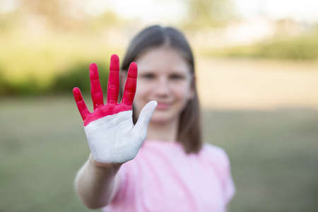 Girl with open hand raised, painted in Indonesia flag color, focus on hand. Girl show stop gesture with hand. Indonesian Independence Day, Hari Kemerdekaan, 17 August. National Day of Monaco 19 Novemberの写真素材