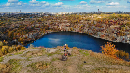 Young woman cycling on bike outdoors aerial view from above. Aerial view of happy sport girl relaxing near beautiful mountains lake from above, sport and fitness conceptの写真素材