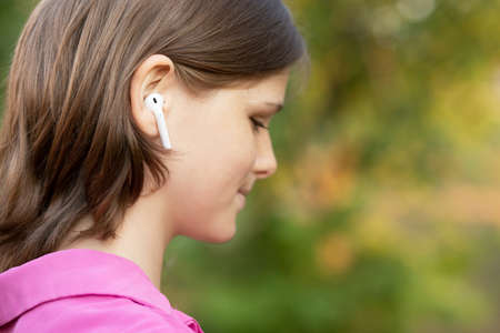 Close up portrait of lovely girl in pink listening to music through wireless earphones outdoors. Young girl smiling happy.の写真素材
