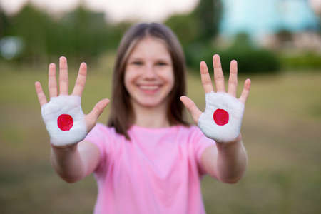 Happy funny smiling child girl show open hand raised painted in Japan flag colors, focus on hands.の写真素材