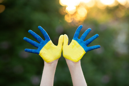 Little school girl showing hands painted in yellow and blue color. Kid hands painted in blue and yellow flag of Ukraine. Ukrainian Independence Flag Day. Constitution day. 24 August. Patriotic holiday. flag of Ukraine. Education, school, art and kid happiness concept.の写真素材