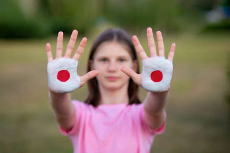 Sad unhappy child girl show open hand raised painted in Japan flag colors, focus on hands.の写真素材