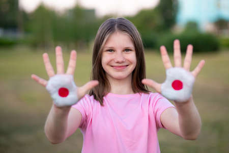 Happy funny smiling child girl show open hand raised painted in Japan flag colors outdoorの写真素材