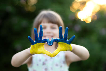 Heart shape with child hands of kid body language for children love, kindness, patriot love concept. Heart hand over sunset sky bokeh background painted in Ukrainian flag colorsの写真素材