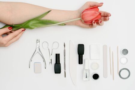 Tools for manicure and womens delicate hand with a red flower tulip on white backgroundの写真素材