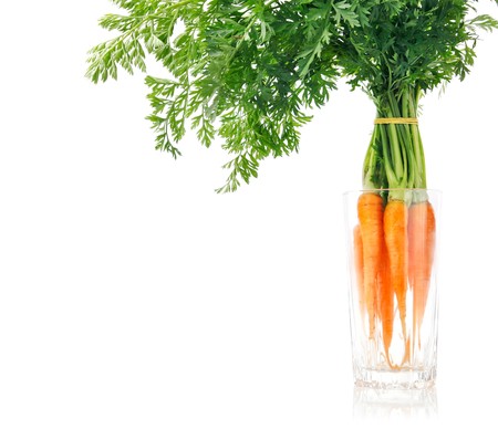 fresh carrot fruits with green leaves in the glass isolated on white backgroundの写真素材