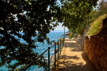Picturesque embankment along resort old town at coast of Adriatic Sea with blue water and waves. Trees with green leaves.の写真素材