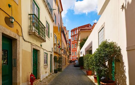 Ancient street of Lisbon old town. Vintage shabby houses with tegular roofs and door, stone paving stones. Sunny summer day.の写真素材