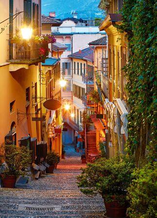 Bellagio village at lake Como near Milan Italy, region Lombardy. Famous street with paving stones stairs and cosy restaurants during sunrise with glowing lanterns and green plants on old houses wallsの写真素材